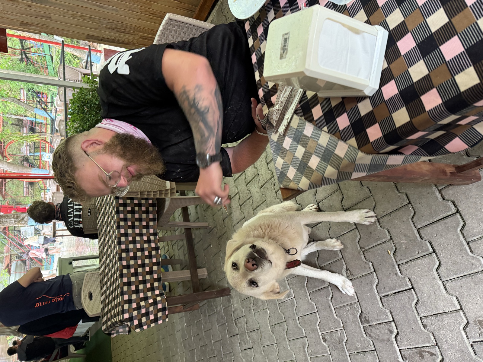 Smiling man at an outdoor cafe table feeding a treat to a dog